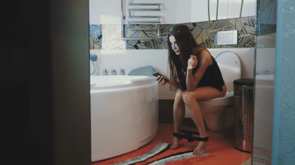 Jeune fille assise sur les toilettes avec smartphone. Sous-vêtements. Fumée cigarette électronique . — Video