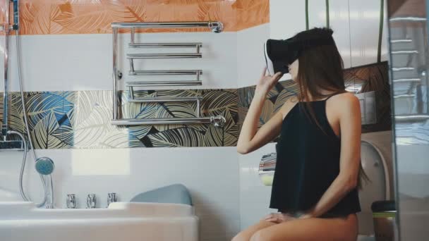 Девушка сидит на унитазе. Смотрю в очки виртуальной реальности. В ванной. Виртуальный мир . — стоковое видео