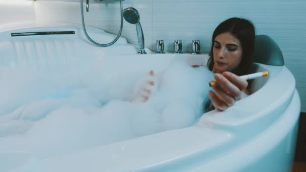 Girl take bath full of foam in bathroom. Smoke electronic cigarette. Bathtub — Stock Video