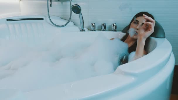 Fille prendre bain plein de mousse dans la salle de bain. Fumer une cigarette électronique. Vapeur — Video