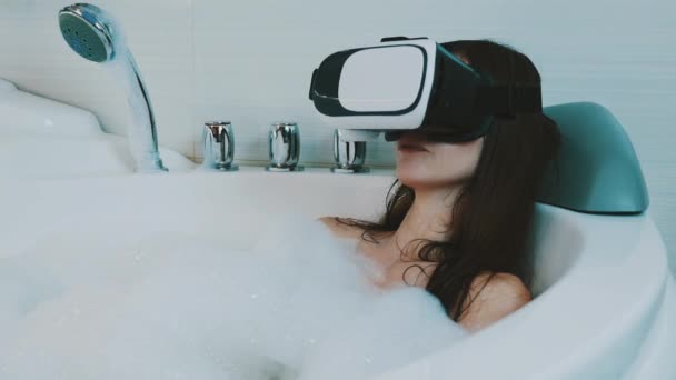 Chica tomar un baño lleno de espuma en el baño con máscara de realidad virtual. Mira a tu alrededor — Vídeos de Stock