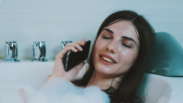 Bruna ragazza fare il bagno pieno di schiuma. Parla al telefono. Rilassati. Ridi. Sorridi — Video Stock