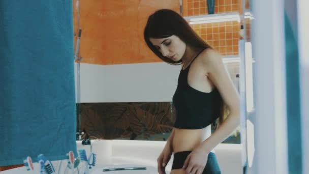 Slim κορίτσι στη μαύρη κορυφή μηρό ελέγχου μπροστά από καθρέφτη στο μπάνιο. Λεία. — Αρχείο Βίντεο