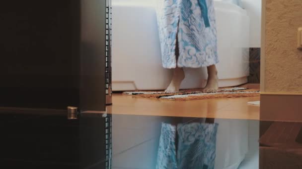Menina em roupão de banho azul levantar-se de banho branco sair do banheiro na ponta dos pés . — Vídeo de Stock