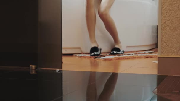 视图的拖鞋的年轻女子从浴站起来，走出浴室. — 图库视频影像