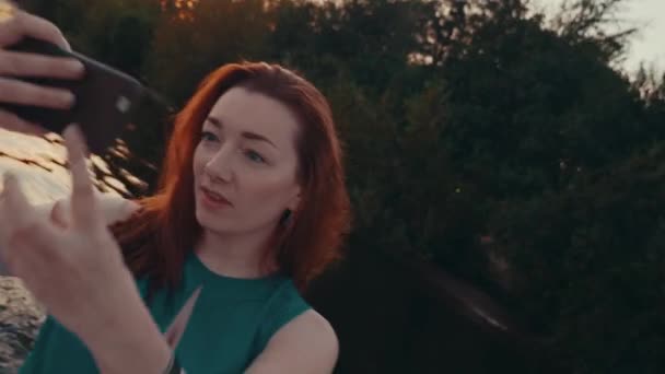 Chica de pelo rojo feliz en vestido turquesa tomar selfie en barco a motor de vela. Puesta de sol — Vídeos de Stock