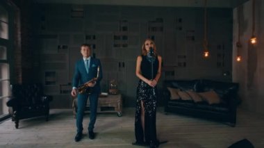 Saksofoncu ile sahnede performans parlayan elbiseli çekici caz vokalisti