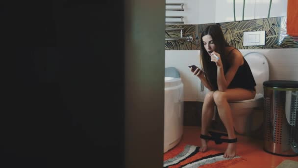 La ragazza si siede sul water. Biancheria intima. Usa lo smartphone. Fumo sigaretta elettronica . — Video Stock