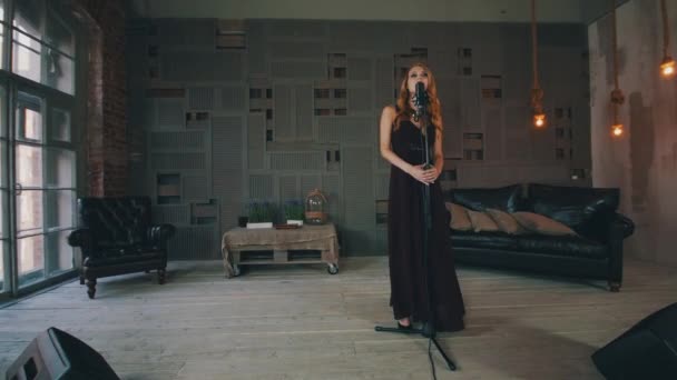 Привлекательный джазовый вокалист в черном платье выступает на деревянной сцене у микрофона — стоковое видео