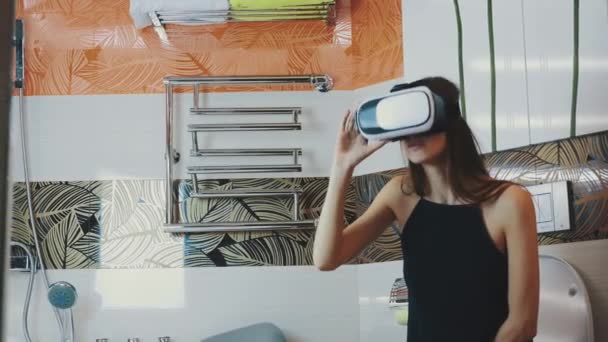 La chica se sienta en el baño. Mirando a su alrededor con gafas de realidad virtual. Nuevas tecnologías — Vídeo de stock