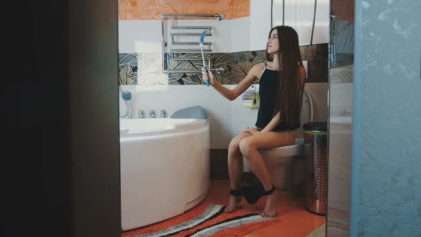 Girl sitting on toilet. Black underwear. Posing for selfie on blue monopod. — Stock Video