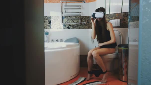 Rapariga sentada na casa de banho. Olhando em óculos de realidade virtual. Dispositivo. Roupa interior — Vídeo de Stock