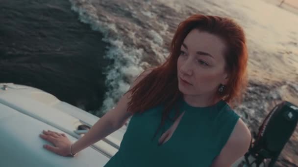 Linda chica de pelo rojo en vestido turquesa en barco a motor. Noche de verano. Agua. — Vídeo de stock