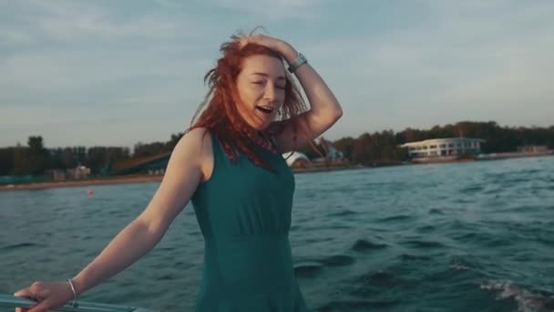 Chica de pelo rojo feliz vestido de color turquesa se ríen en barco a motor. Muestra lengua. Diversión — Vídeos de Stock
