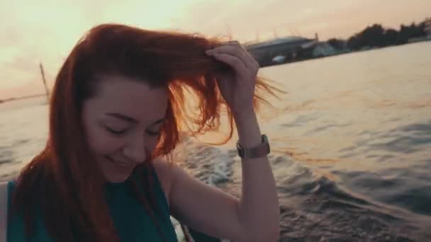 Молода дівчина з червоного волосся в бірюзовій сукні на моторному човні. Захід сонця. Подивіться в камеру — стокове відео