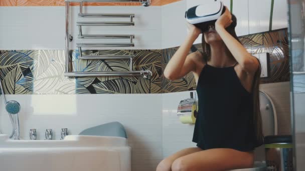 La ragazza si siede sul water. Guardando in occhiali di realtà virtuale. In bagno. Gioco virtuale . — Video Stock