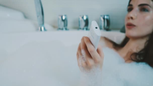 Chica tomar un baño lleno de espuma en el baño. Cambiar música por controlador. Bostezando — Vídeo de stock