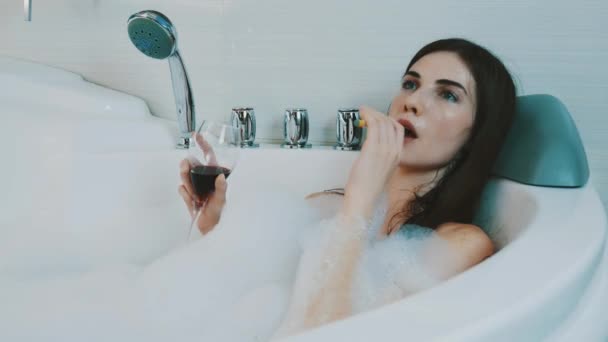 Κορίτσι με κόκκινο κρασί ποτήρι σε μπανιέρα γεμάτη από αφρώδες υλικό. Ηλεκτρονικό τσιγάρο κάπνισμα. — Αρχείο Βίντεο