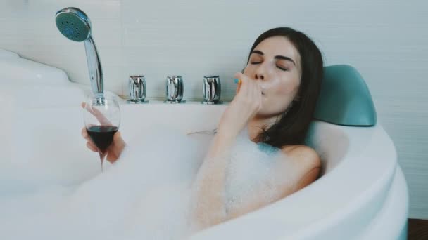 Ragazza bere vino rosso in bagno pieno di schiuma. Fumare sigaretta elettronica. Riposo — Video Stock