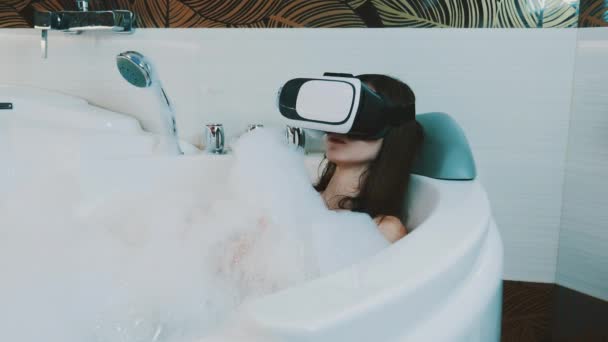 Girl relax in bath full of foam in bathroom with virtual reality glasses on head — Stock Video