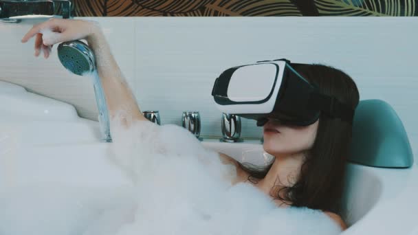 Girl take bath full of foam in bathroom. Looking in virtual reality glasses. — Stock Video