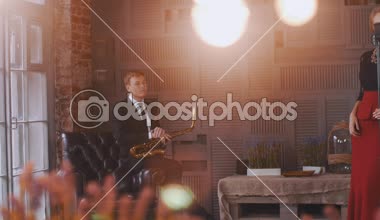 Caz Vokal mikrofon, retro tarzı elbiseli. Saksofoncu sit sandalyede.