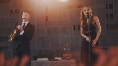 Siyah elbiseli çekici caz vokalisti saksofoncu ile sahnede dans gerçekleştirmek