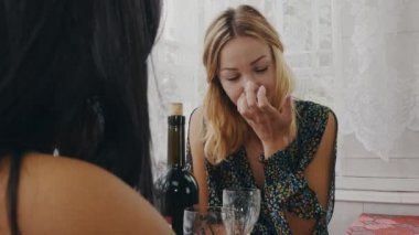 Ülkenin evin terasında masada sohbet esmer ve sarışın kız.