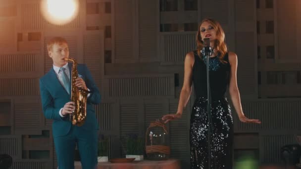 Jazz vocalist in glare dress and saxophonist in blue suit perform on stage. Duet — Stock Video