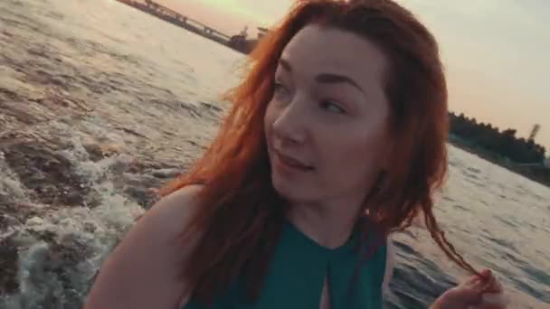 Молода дівчина в бірюзовій сукні торкається волосся на моторному човні. Подивіться на захід сонця. романтичний — стокове відео