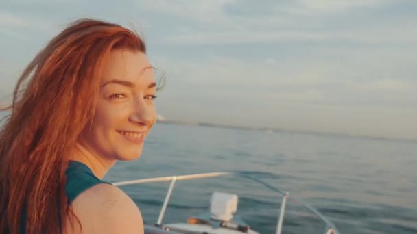 Glücklich rote Haare Mädchen in türkisfarbenem Kleid steuern Motorboot. schöner Sonnenuntergang. — Stockvideo