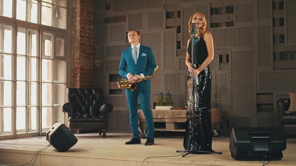Jazz vocalist in schittering jurk en saxofonist in blauwe pak op het podium. Dans. Zingen — Stockvideo