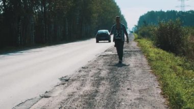 Yol boyunca sırt çantası yürüyüş üzgün adam. Otostop. Yukarı başparmak. Gezgin.