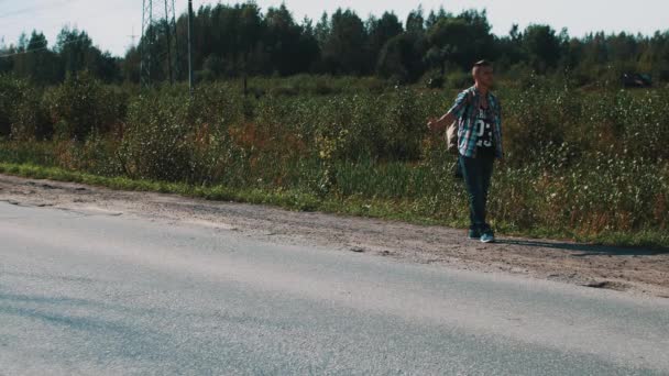 O homem fica na estrada no campo. A pedir boleia. Polegar para cima. Fuma cigarro. Viagens — Vídeo de Stock