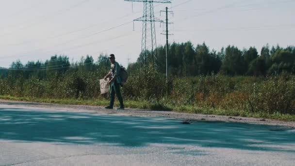 Jongen lopen langs de weg met kartonnen plaat met teken stad. Liften. — Stockvideo