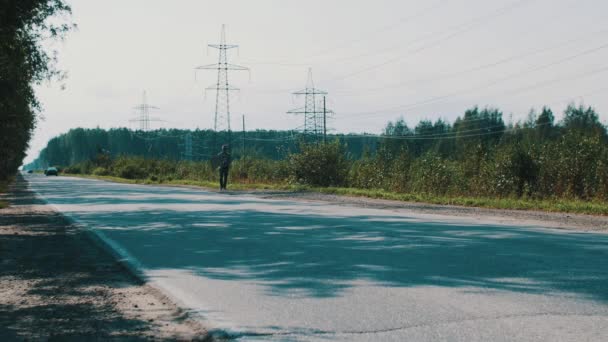 Człowiek spacerem wzdłuż drogi w okolicy z płytą karton. Autostop. Kciuk w górę — Wideo stockowe