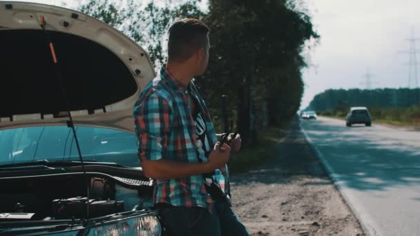 Homem perturbado no carro quebrado com capota aberta na estrada no campo. Óculos de sol . — Vídeo de Stock