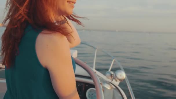 Red hair girl in turquoise dress steer motor boat. Beautiful sunset. Evening. — Stock Video
