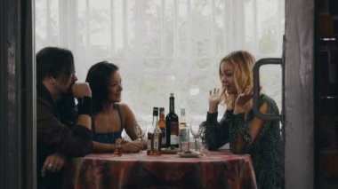 İki kız ve adam masada ülkenin evin terasında içecekler ile sohbet.