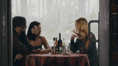 İki kız ve adam masada ülkenin evin terasında içki ile sohbet.