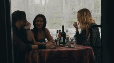 İki kız ve adam masada ülkenin evin terasında içki ile sohbet.