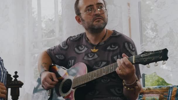 Hombre barbudo adulto toca la guitarra acústica en la terraza de la casa de campo. Verano . — Vídeos de Stock