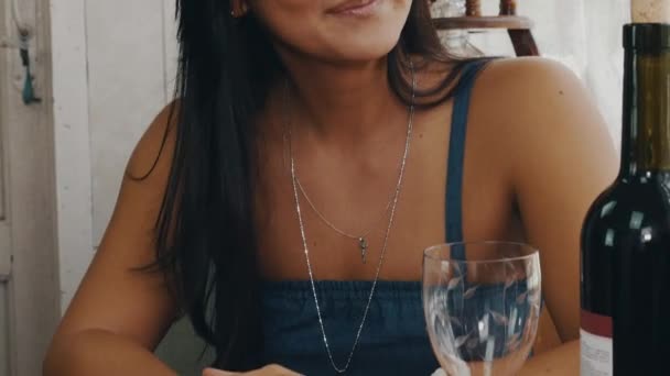 Брюнетка болтает за столом с бутылкой красного вина на террасе загородного дома — стоковое видео