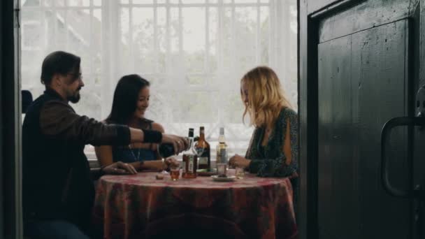 Dos chicas y un hombre hablando en la mesa. Beber vino tinto en la terraza de la casa de campo . — Vídeos de Stock