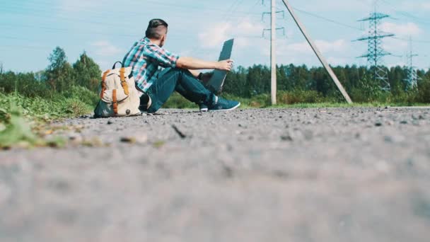 Fiatal férfi ül, stoppolás Road, vidéken karton táblával a kezében. — Stock videók