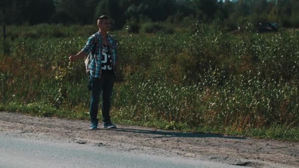 Der Mensch bleibt auf dem Land auf der Straße. Per Anhalter. Daumen hoch. Reisende. Sommertag — Stockvideo