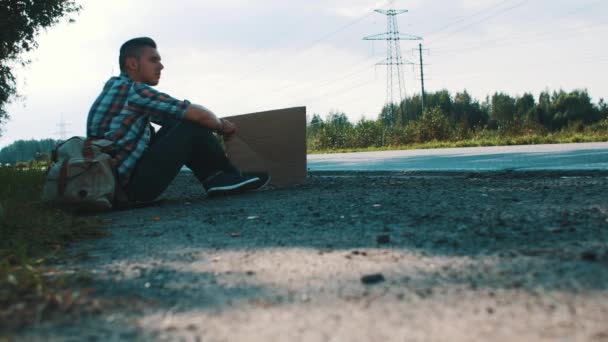 L'uomo siede a strada in campagna con piatto di cartone. Autostop. In attesa di aiuto . — Video Stock