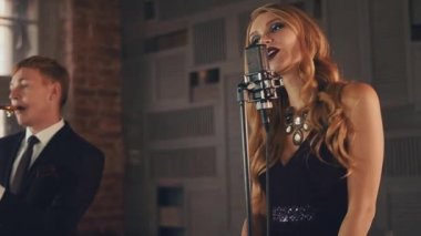 Elbiseli caz vokalist ve takım elbiseli saksafoncu sahnede performans sergiliyor. Retro tarzı