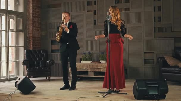 Jazz vocalist click fingers on stage, saxophonist in black suit plays. Duet. — Stock Video