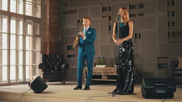 Jazzový zpěvák v oslnivérním oděvu a saxofonista v modrém obleku na scéně. — Stock video